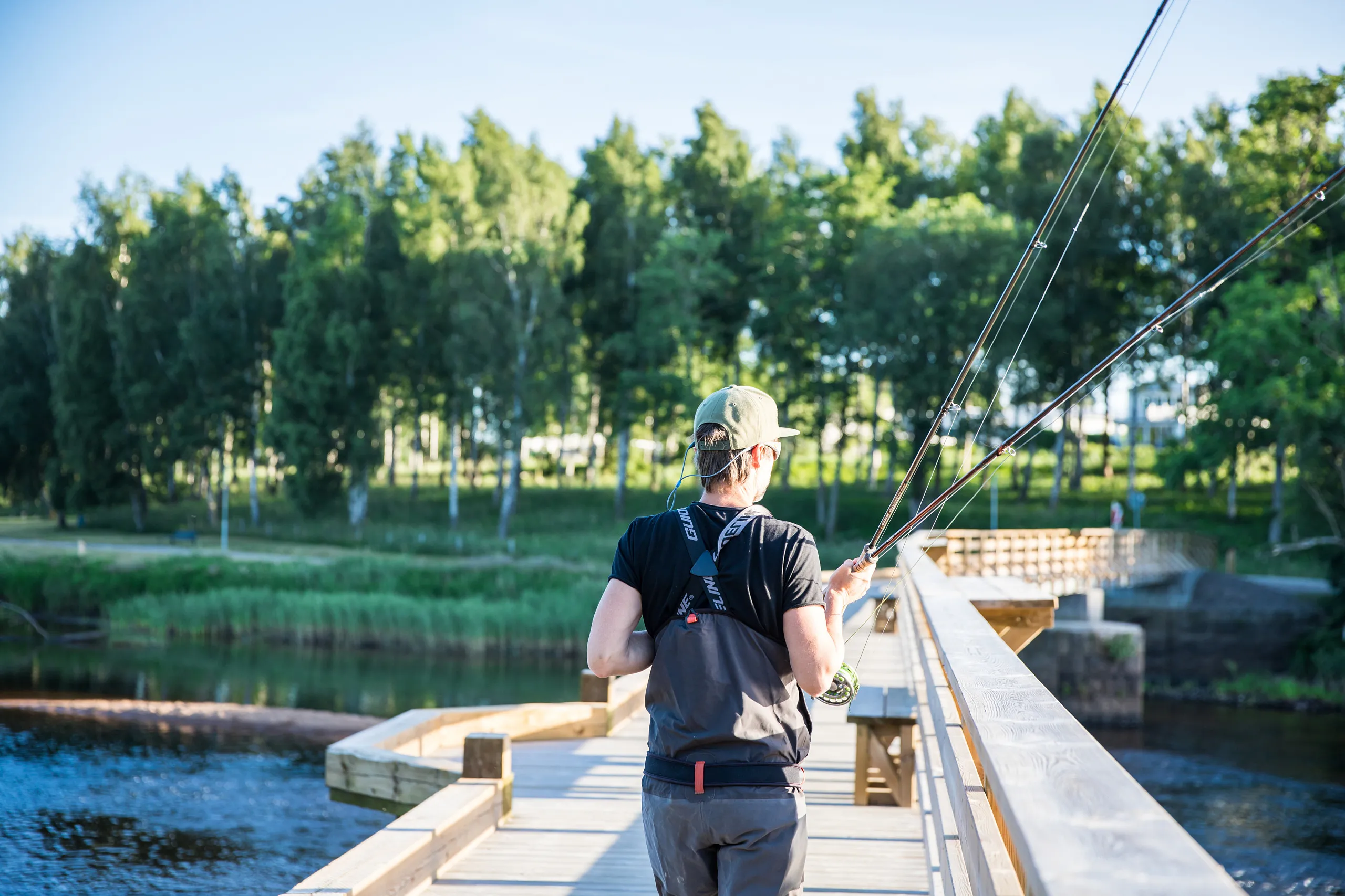 Man som går på bro med fiskeutrustning i handen.